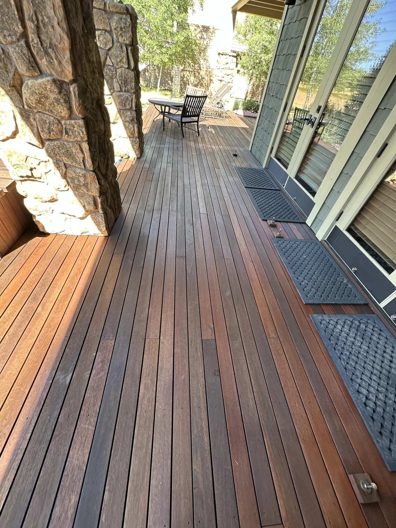 Timber deck along a covered porch with stone columns and glass doors