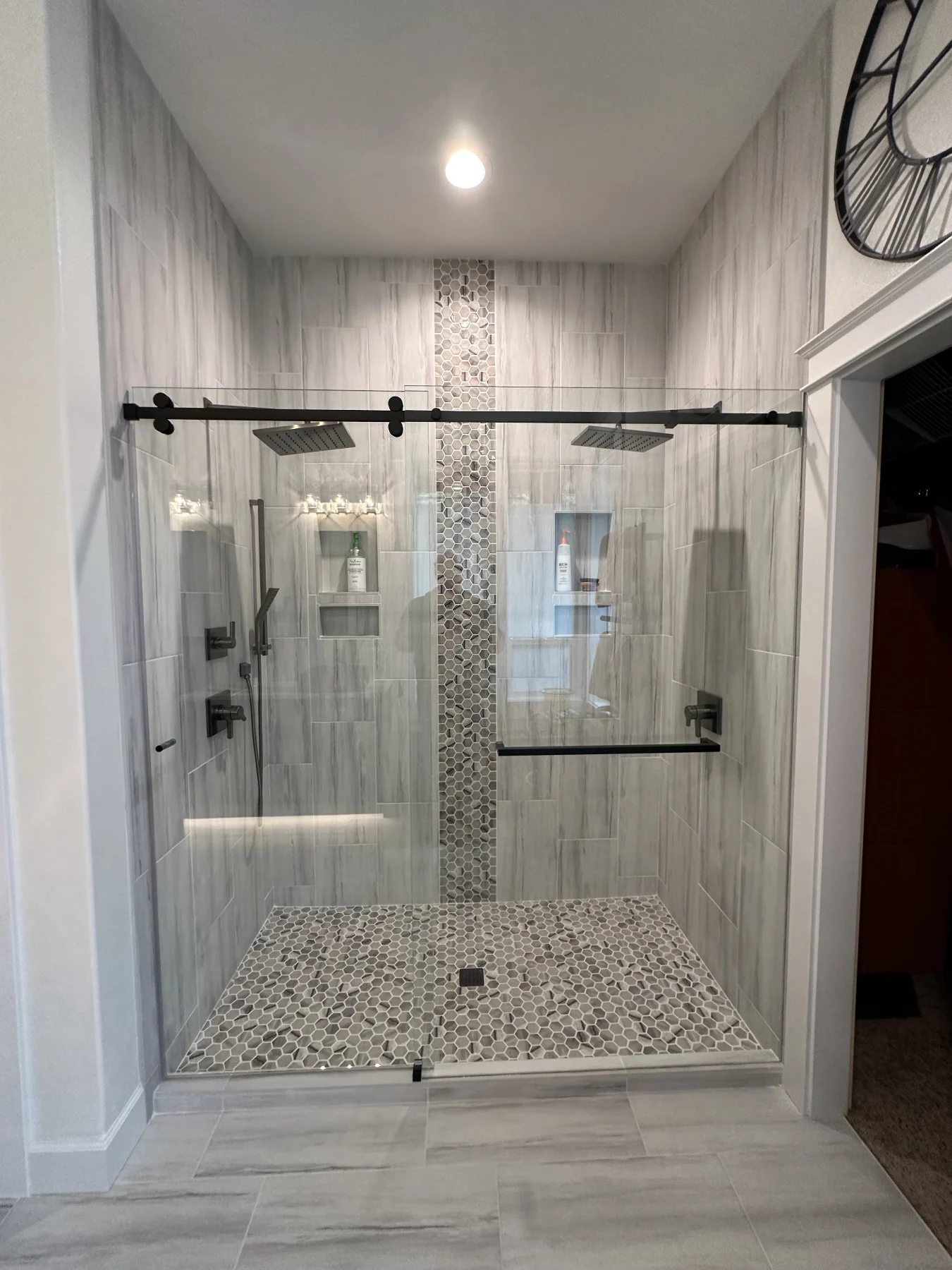 Glass-enclosed shower with two black rain heads, pale wall tile and a hexagonal mosaic floor