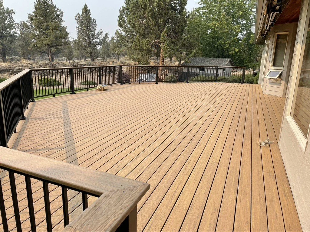 Expansive wood-tone deck with black railing overlooking a pine landscape