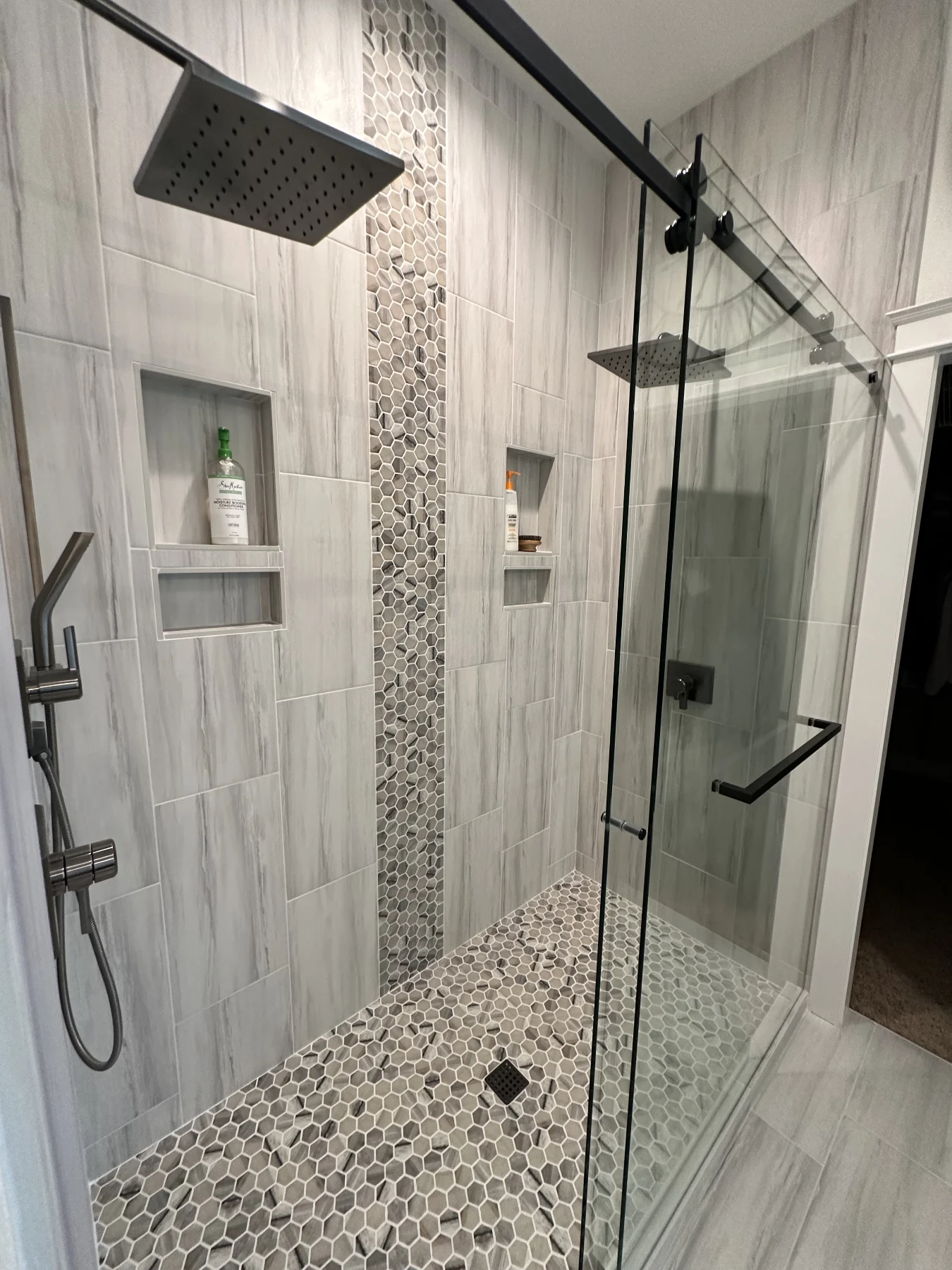 Close view of two rain shower heads, recessed niches and hexagonal mosaic tile behind glass