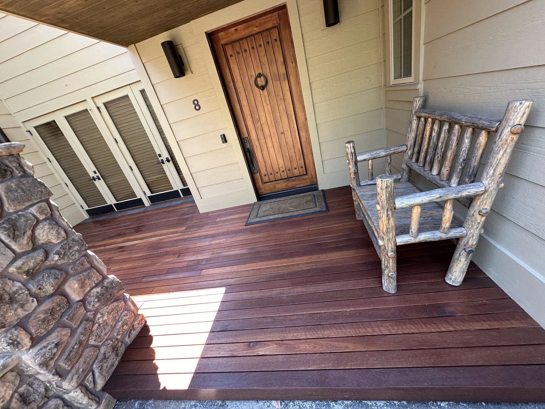 Timber porch decking beside a wood front door, pale siding and a rustic chair