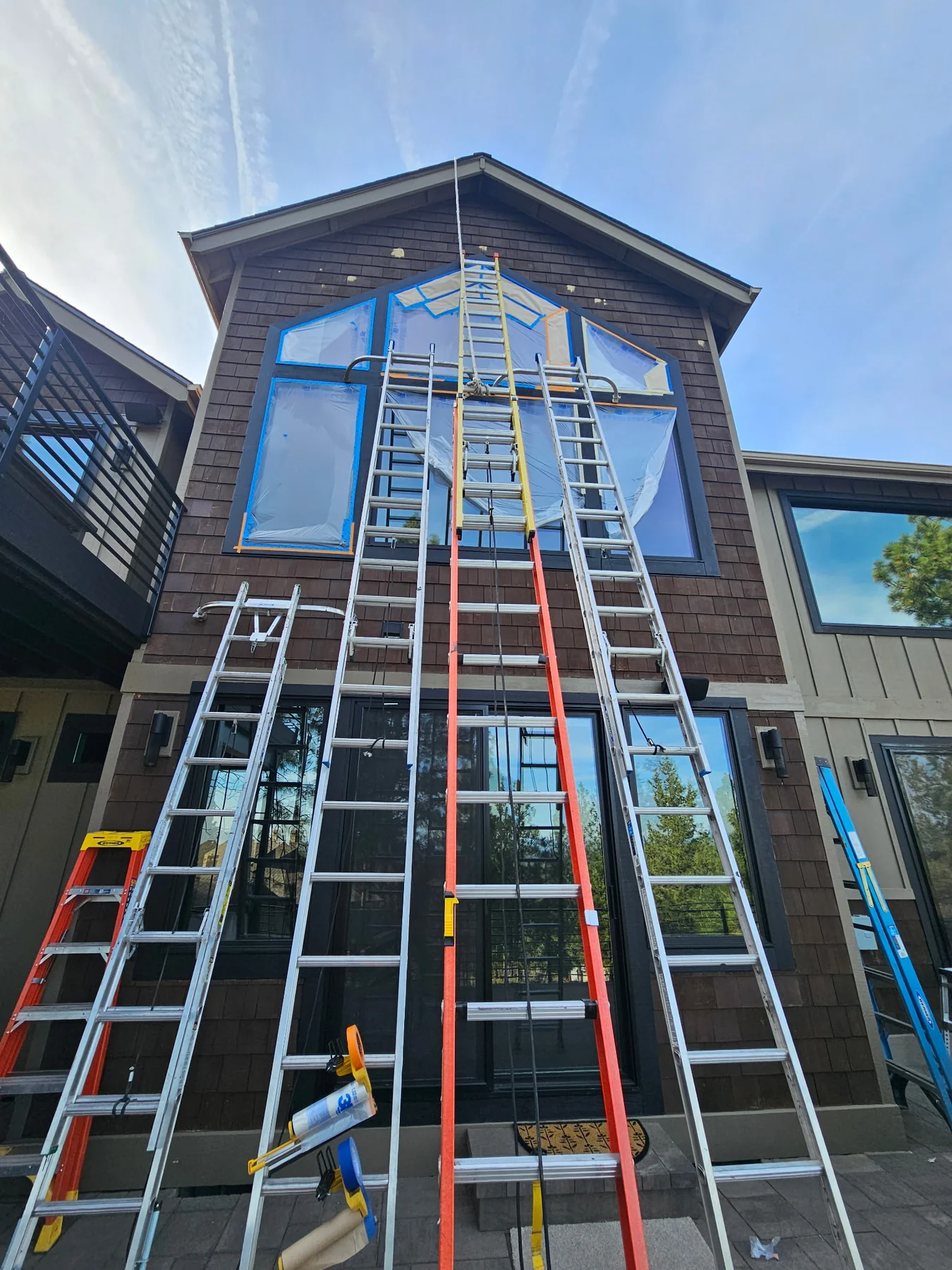 Tall exterior windows masked for painting, with ladders against the home